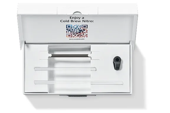 Geöffnete Zubehörbox ‘Cold Brew Nitro’ von JURA mit QR-Code im Deckel; darin drei Glasröhrchen, eine Halterung und ein schwarzer Adapter.